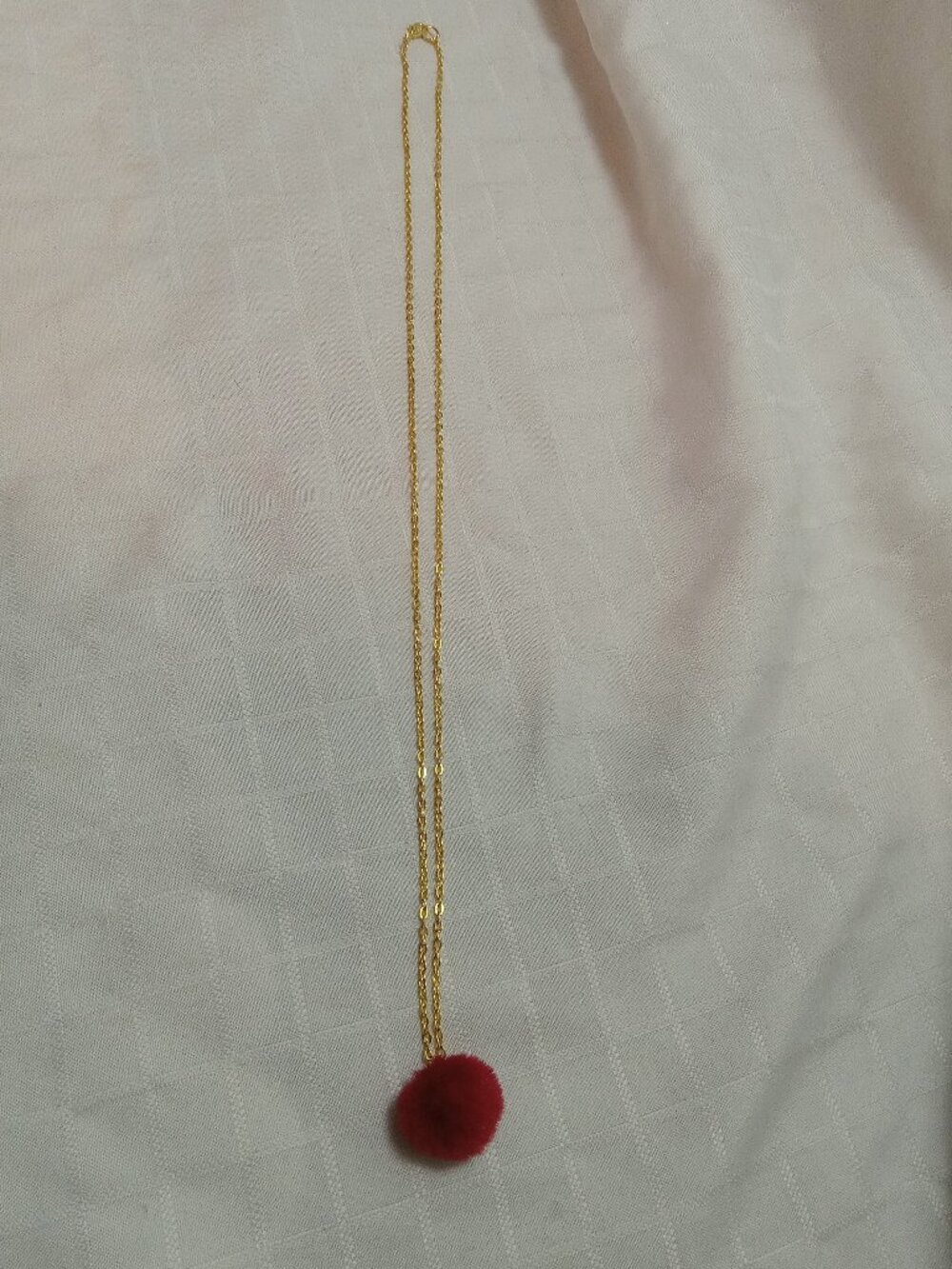 Handmade necklace with a small pom-pom and gold-colored accent hooks and chains